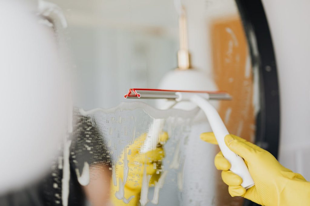 pexels-photo-4239145 Anonymous person in yellow rubber gloves wiping water by squeegee from mirror in bathroom