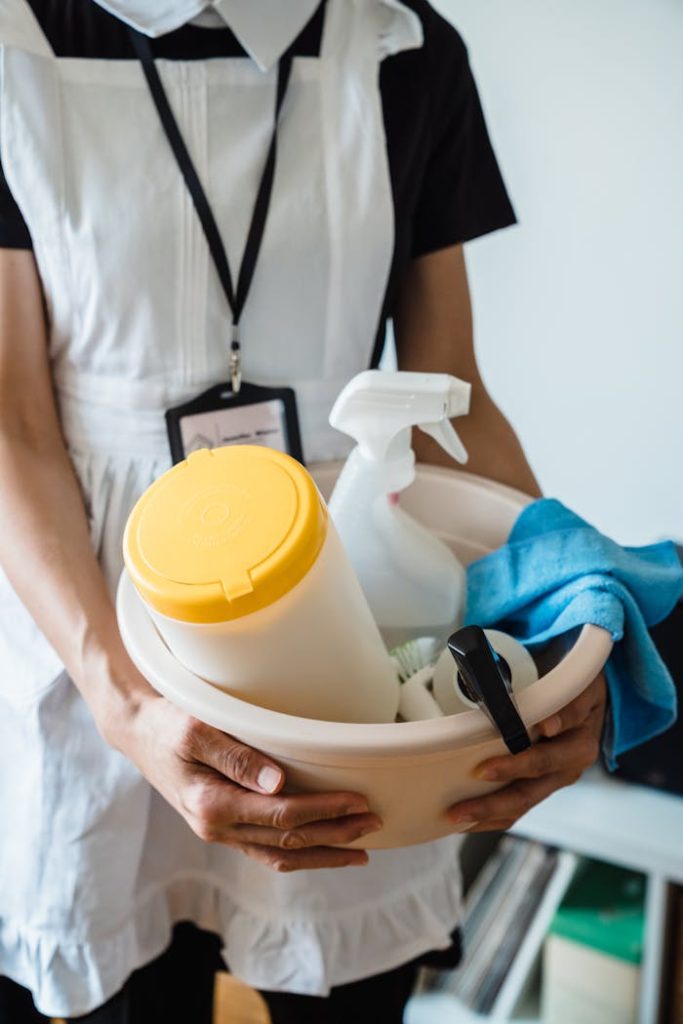 pexels-photo-9462663 A uniformed cleaner holding a basin with cleaning supplies indoors. Ideal for cleaning and sanitation themes.